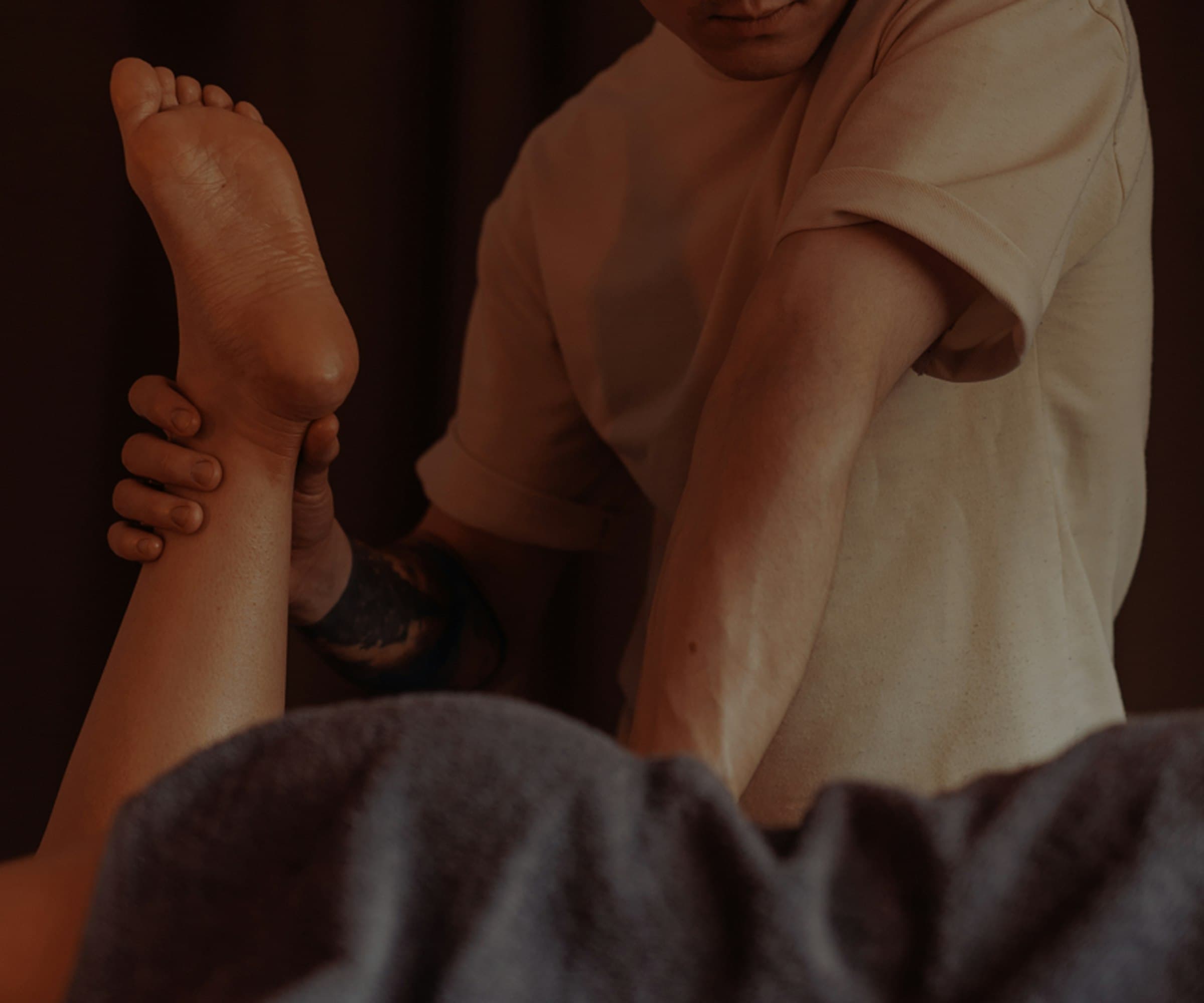 Praticienne travaillant en douceur la jambe d'une cliente dans une pièce sombre et feutrée