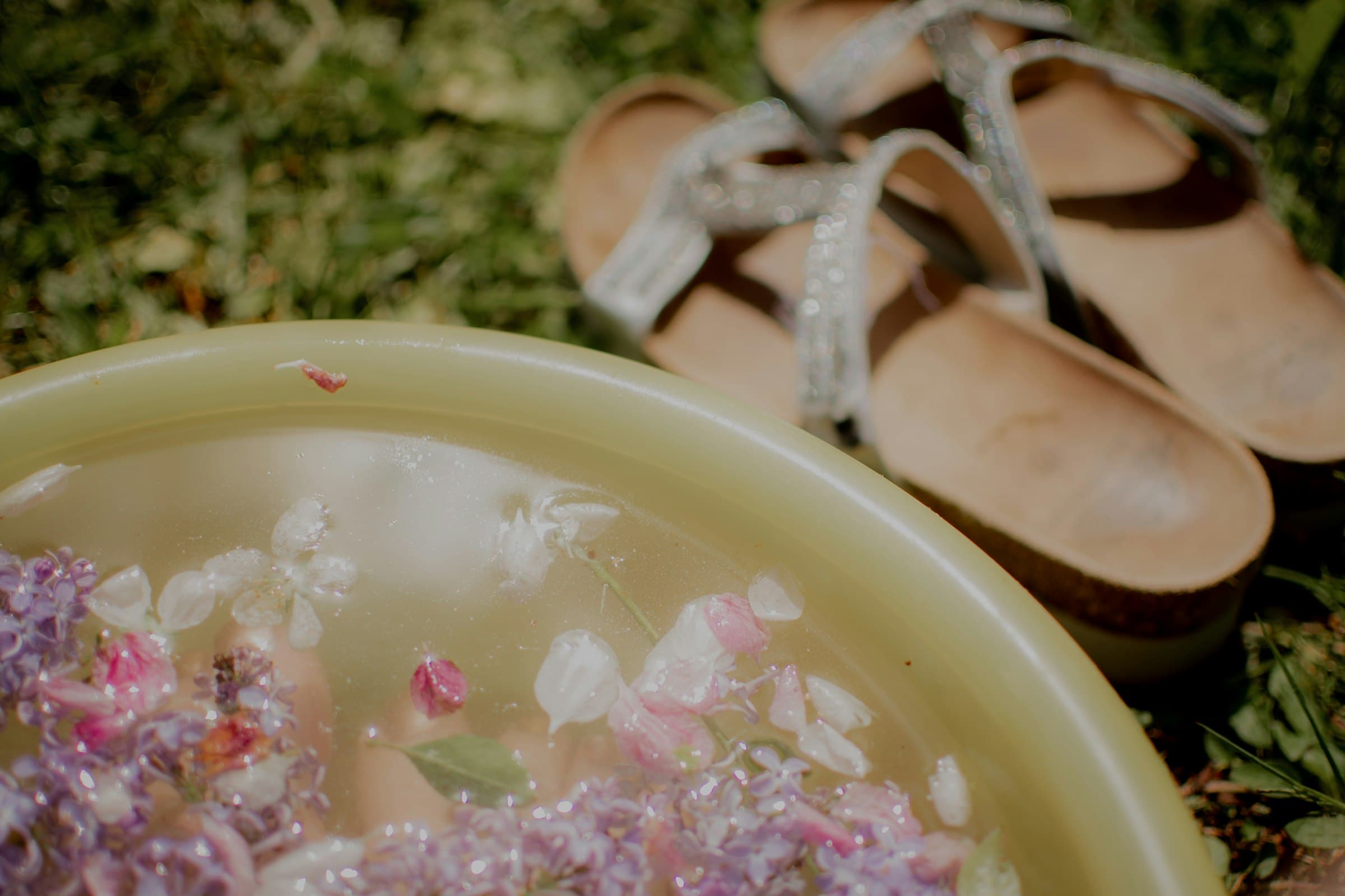Bain de pieds aux fleurs flottantes à côté de sandales sur l'herbe
