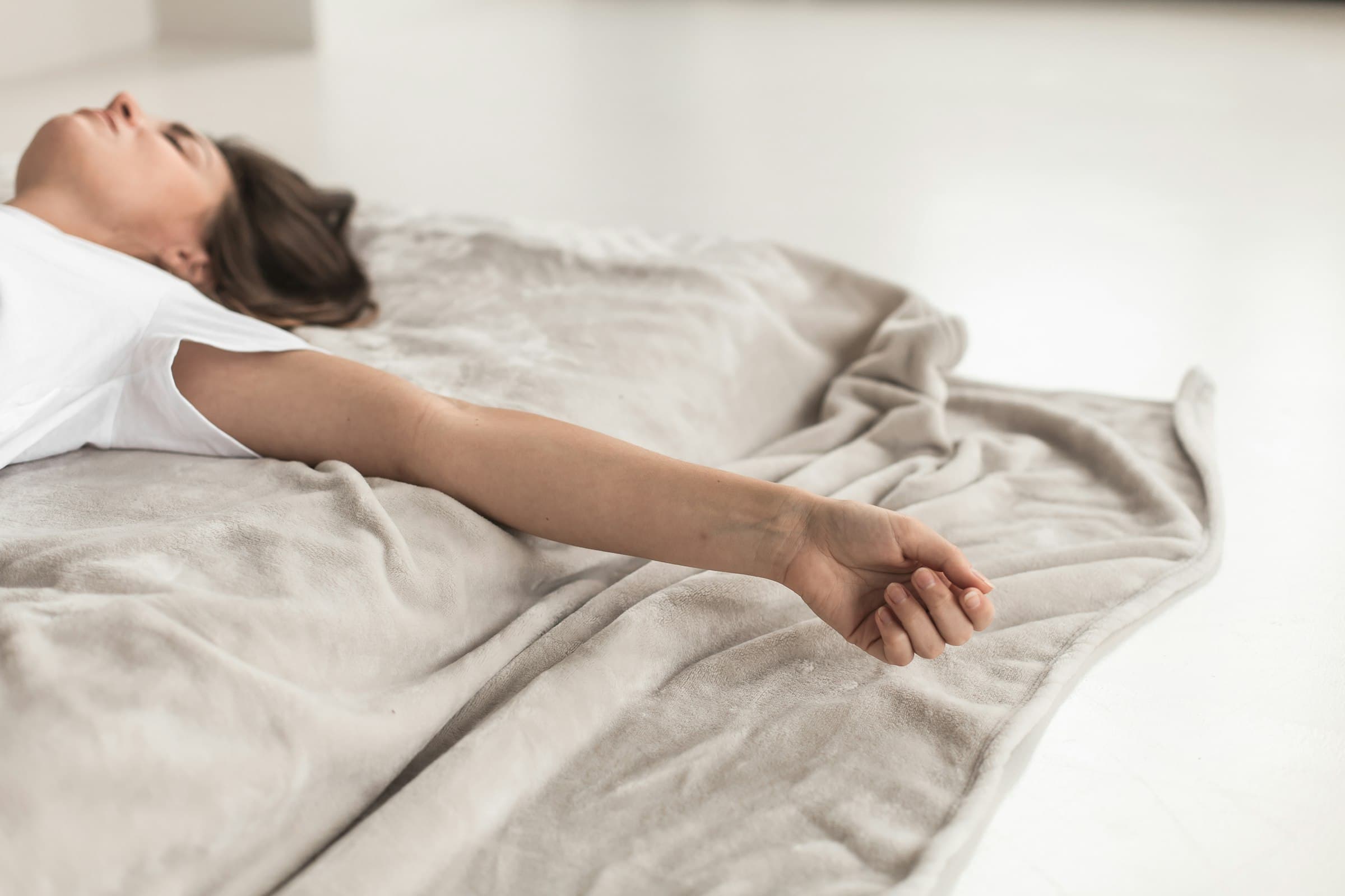 Femme allongée sur une couverture douce, les yeux fermés, respirant calmement