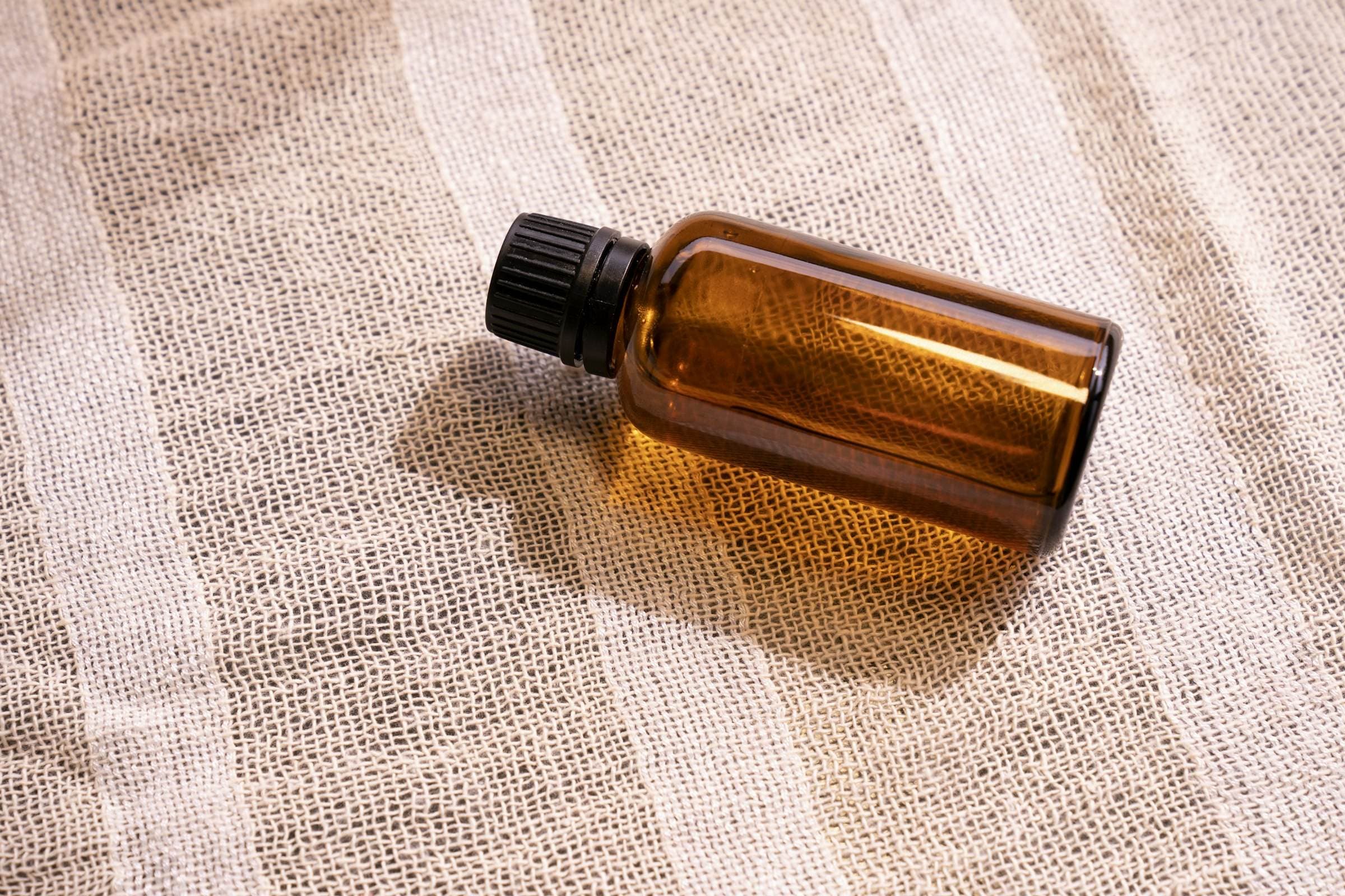 Flacon d'huile en verre ambré posé sur un coton tissé